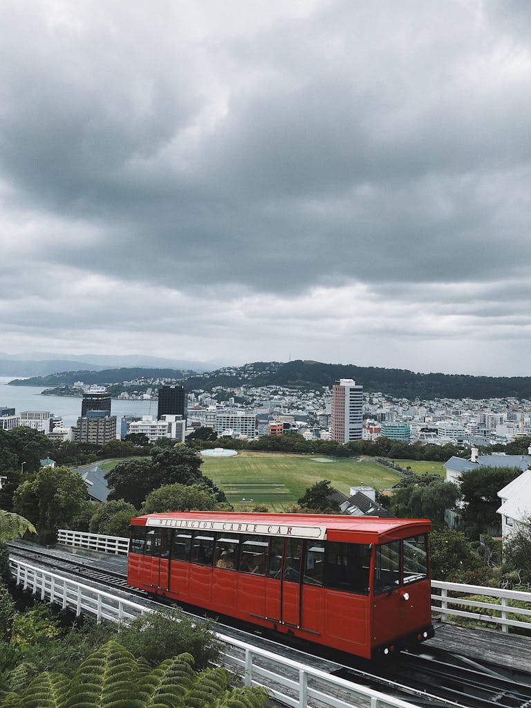 Red cable car on tracks with panoramic view of Wellington cityscape.