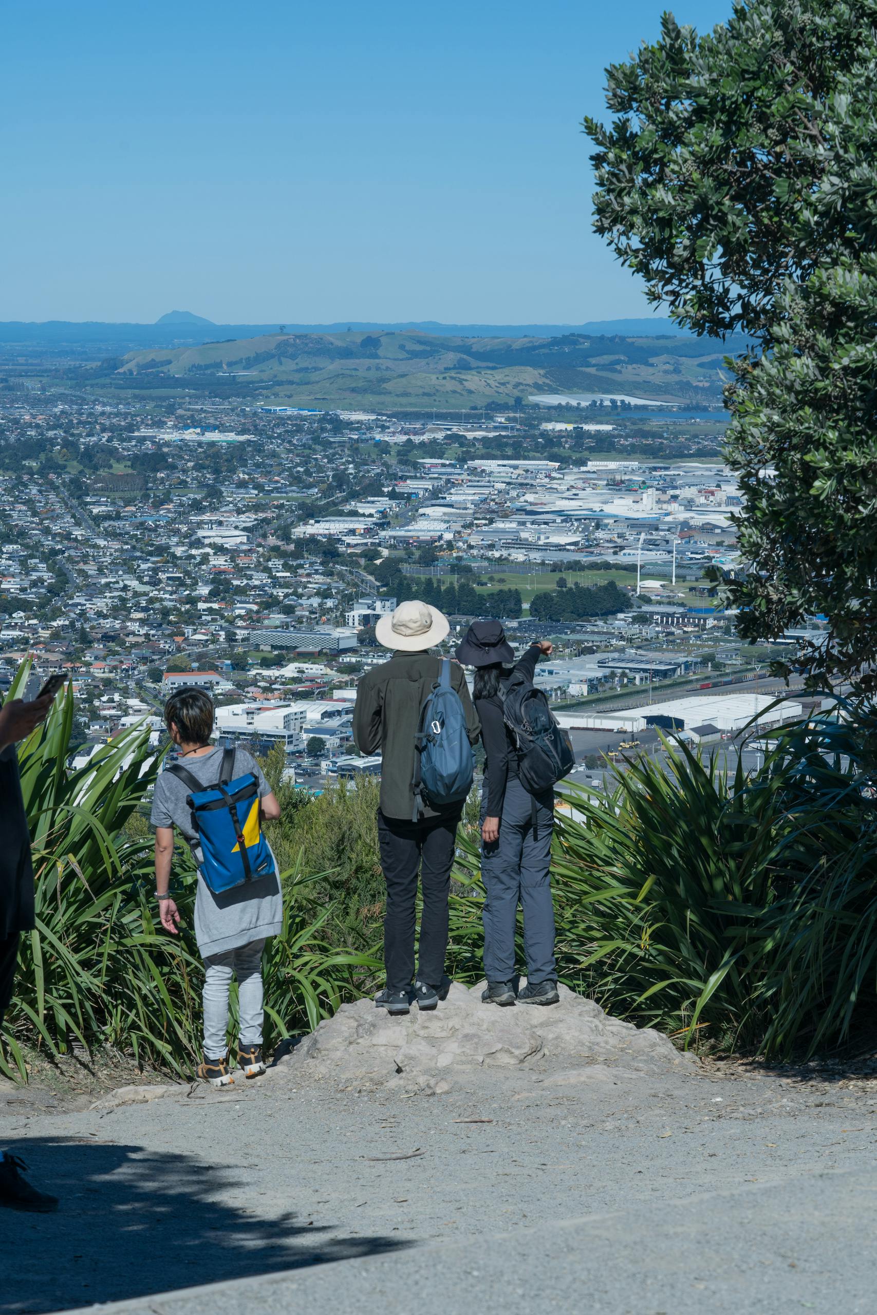 Three hikers admire the stunning cityscape view from Mount Maunganui, New Zealand.